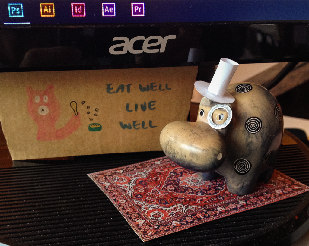 A small statue of a hippo, in front of a computer monitor.