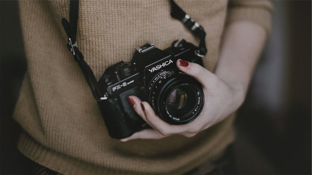 A feminine hand gripping the lense of a Yashica camera around their neck.