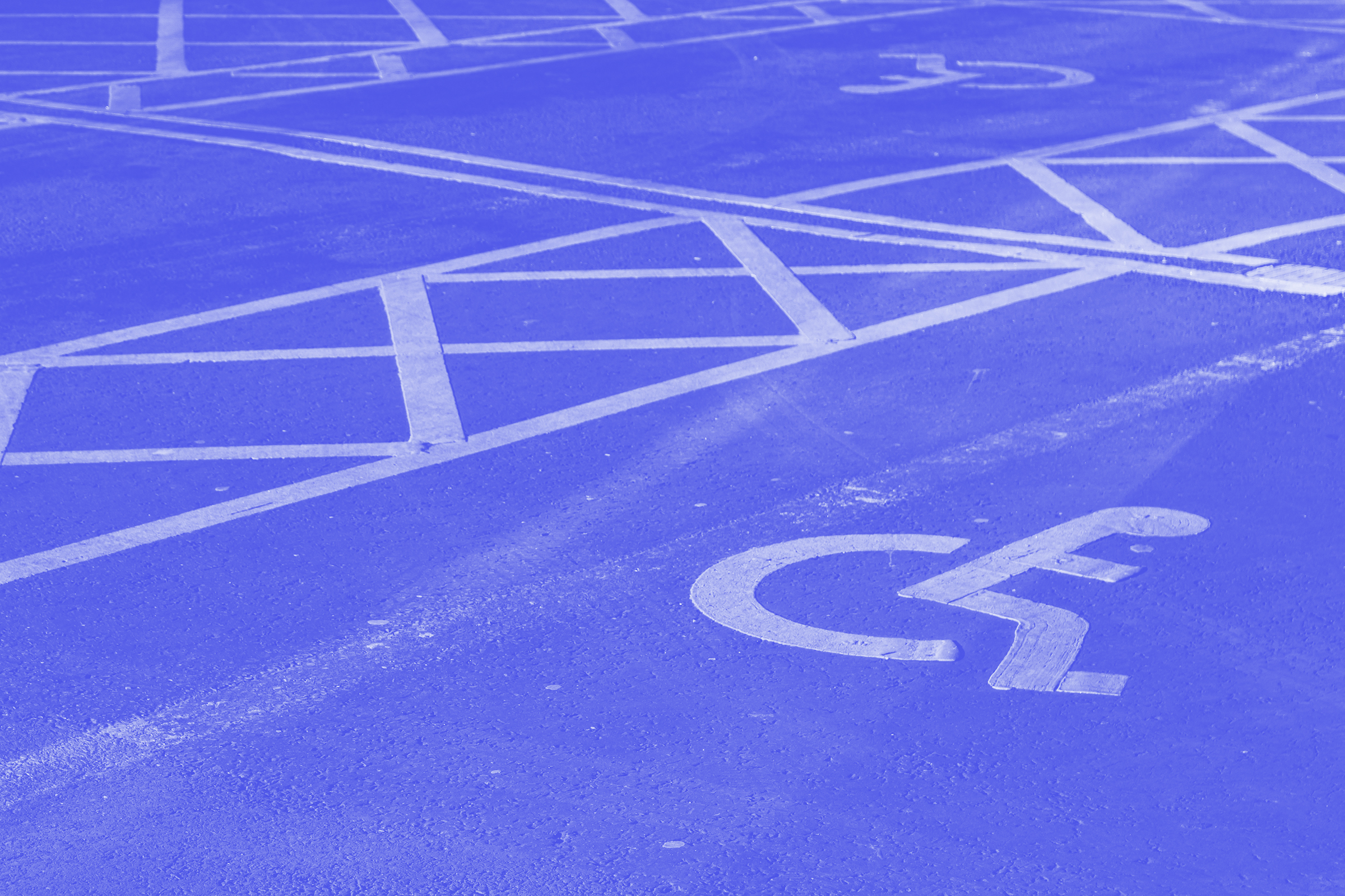 ~Photo by Jakub Pabis Photograph of an accessibility icon on a public roadway. White crosswalk lines appear alongside. ~Photo by Jakub Pabis